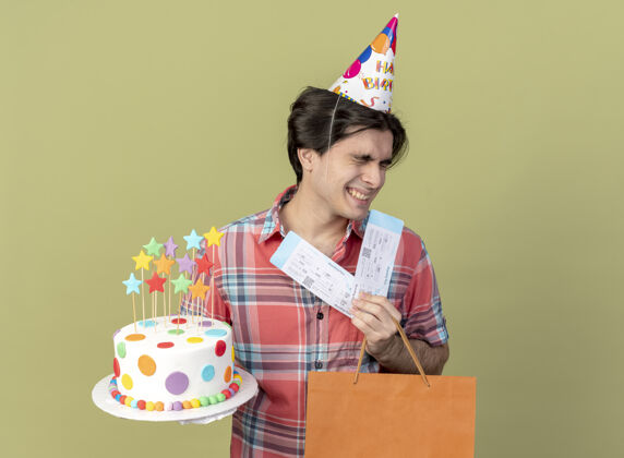橄榄高加索帅哥戴着生日帽 手里拿着纸购物袋 机票和生日蛋糕蛋糕绿色穿