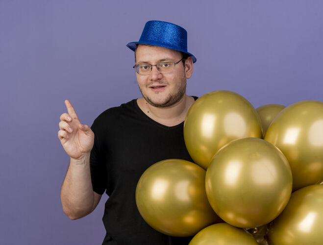请高兴的成年斯拉夫人戴着眼镜 戴着蓝色派对帽 站着氦气球蓝色成人气球