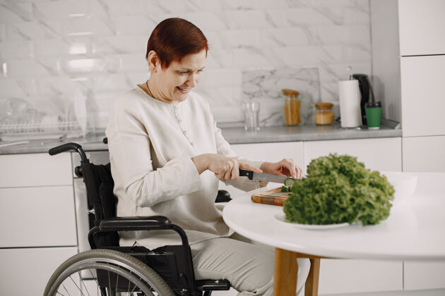 吃饭轮椅上的老妇人在厨房做饭残疾人老人砍微笑