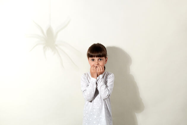 恐惧蜘蛛恐惧症一头黑发 墙上有蜘蛛的影子 吓坏了小女孩 一双吓坏了的大眼睛直视着小女孩 咬着她的指甲 穿得很随意恐惧色调害怕