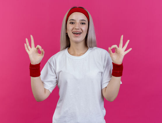 头带快乐的年轻白种人运动女孩戴着背带戴着头带和腕带双手手势ok手势运动腕带粉色