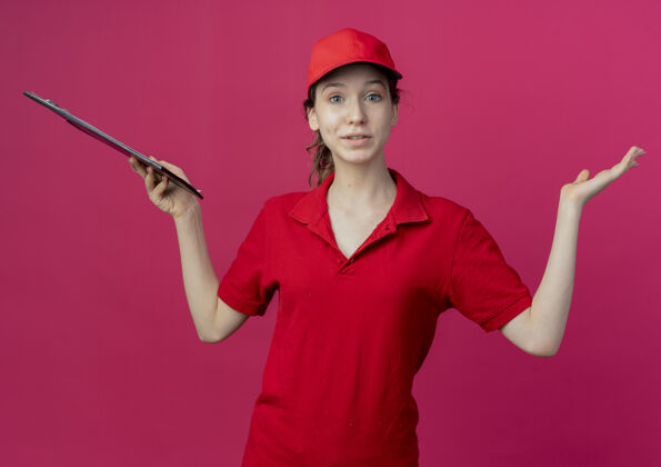 印象令人印象深刻的年轻漂亮的送货女孩在红色制服和帽子举行剪贴板 并显示在深红色的空间空手举行剪贴板漂亮