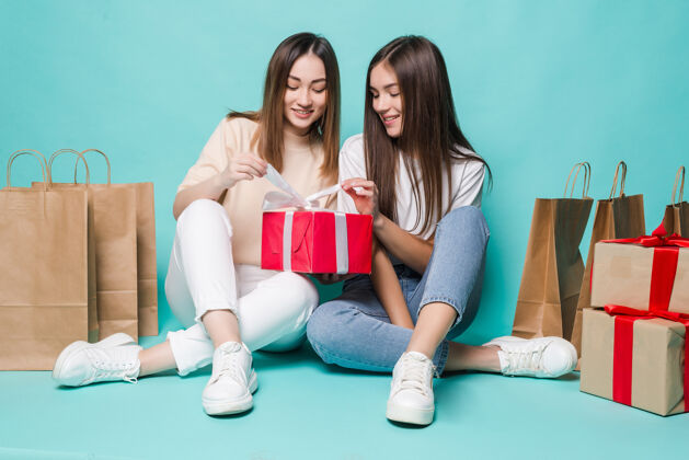 赛车微笑的年轻两个女孩坐在地板上购物袋和打开礼物的绿松石墙上惊喜衣服情感