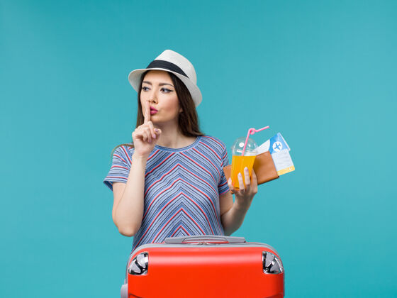 果汁前景：度假中的女人拿着她的红包 拿着蓝色背景的机票和果汁 旅行中的女人微笑女航行