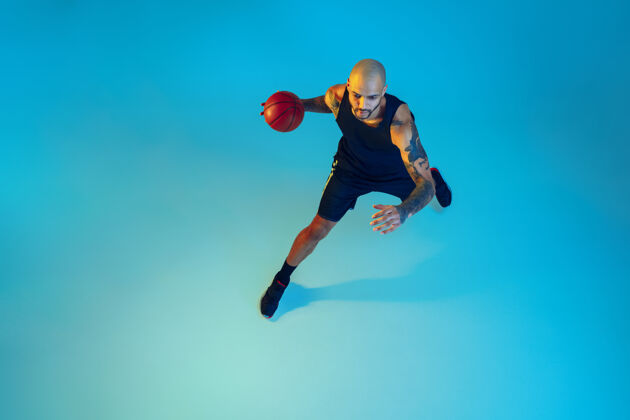 肌肉年轻的篮球队员穿着运动服训练 在运动中练习 在霓虹灯下的蓝色墙壁上运动霓虹灯健康篮球