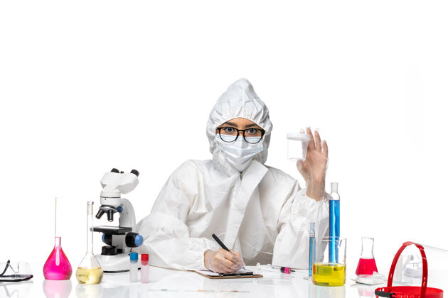 化学正面图身穿特殊防护服的年轻女化学家拿着空烧瓶 在白桌子上写着实验室病毒-化学病毒健康专业面具保护