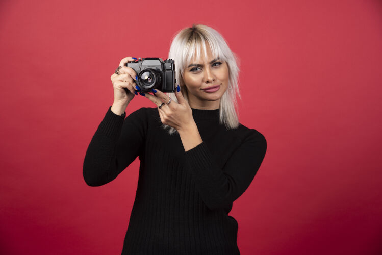 拍摄年轻女子用红色背景的照相机拍照高质量的照片年轻人手持女性