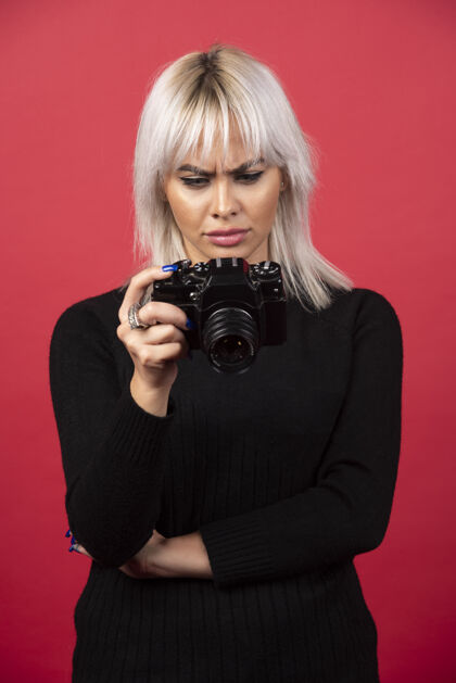 拍摄一个年轻的女人在看一个红色背景的相机高质量的照片姿势女性化手持