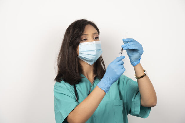 注射器戴着医用面罩和手套的年轻医生在白色背景上准备注射器高质量照片工人职业妇女