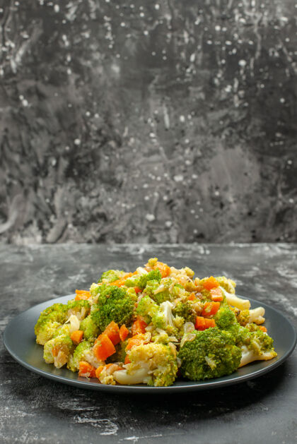 花椰菜健康餐的垂直视图 西兰花和胡萝卜放在带刀叉的黑色盘子上晚餐菜肴食物