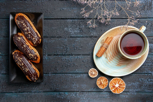 杯子俯视图左侧矩形板上的巧克力蛋糕 右侧黑色木桌上的一杯茶 柠檬干和肉桂 空间宽敞肉桂色左侧茶