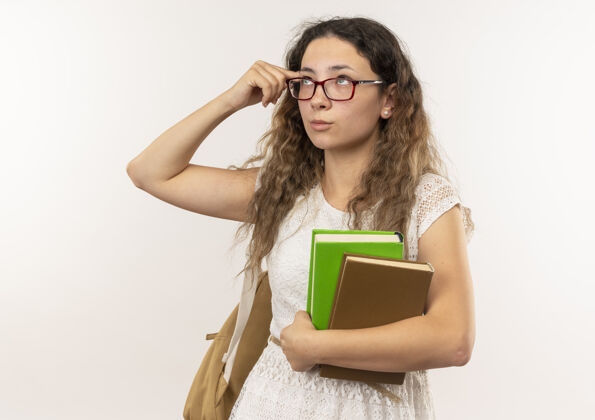 人体贴的年轻漂亮的女学生戴着眼镜背着书包抬起头把手指放在隔离在白色墙上的太阳穴上脸背包