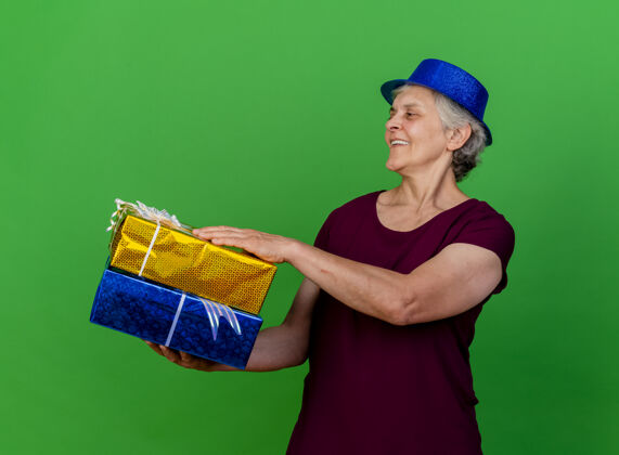 女人微笑着戴着派对帽的老太太拿着礼盒 看着绿色的一面盒子壁板帽子