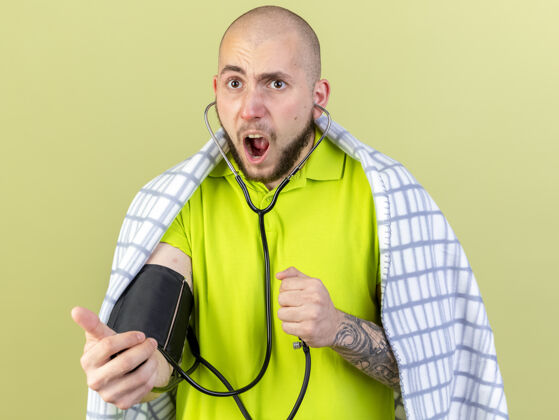 压力恼怒的年轻白种人病人用格子布测量血压计在橄榄绿上疾病绿色测量