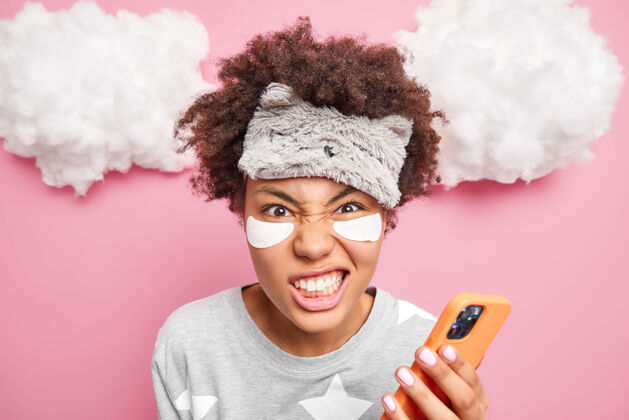 黑发恼怒的女人咬牙切齿被激怒是因为什么东西在眼睛下面贴补丁穿着睡衣用手机上网交流发短信信息手机女人