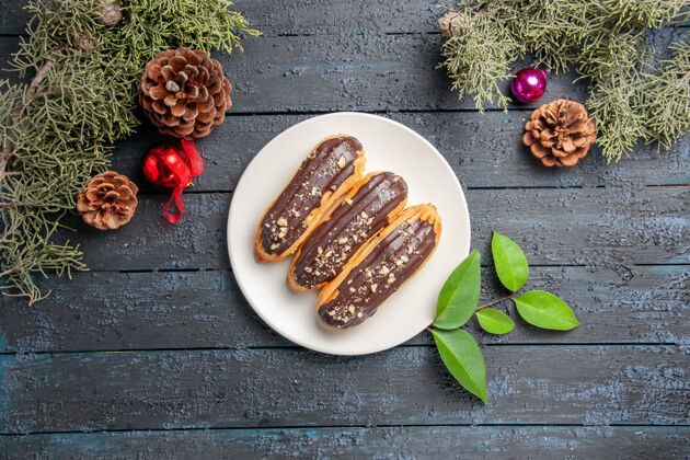 午餐俯视图巧克力eclairs在椭圆形板锥圣诞玩具冷杉树叶在黑暗的木制地面与自由空间盘子木头餐厅