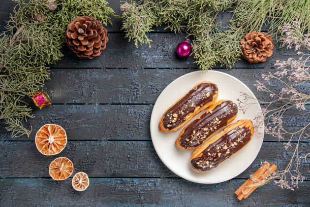 烹饪俯瞰巧克力eclairs白色椭圆形板冷杉树枝和锥圣诞玩具干橙子肉桂黑木桌与自由空间木头桌子圣诞节