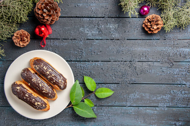 午餐俯瞰巧克力eclairs在椭圆形板锥圣诞玩具冷杉树叶和月桂叶在黑暗的木制地面与自由空间树叶顶部玩具