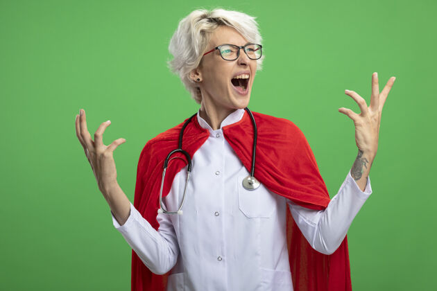 女人穿着医生制服的兴奋的斯拉夫超级英雄女人 戴着红斗篷和戴着眼镜的听诊器眼镜举起壁板