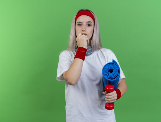腕带自信的年轻白人运动女孩戴着背带和头带哑铃垫子信心