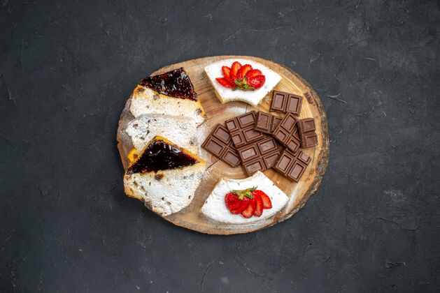 盘子俯瞰美味的蛋糕片与草莓和巧克力酒吧在黑暗的表面巧克力馅饼食物