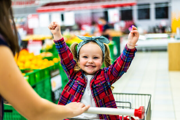小女孩漂亮的妈妈在超市的手推车里抱着她的小女孩手推车超市购物