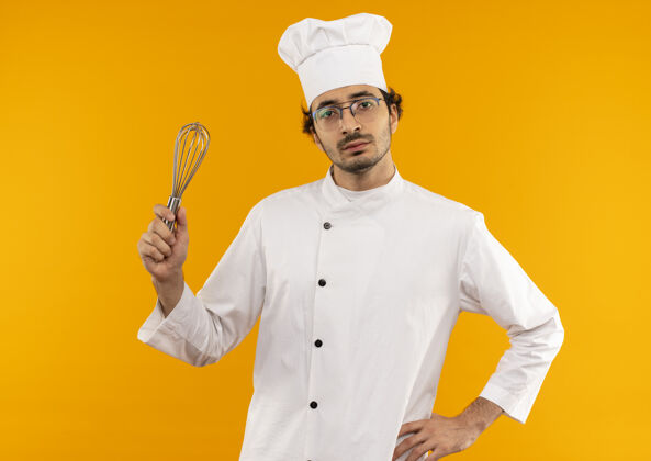厨师自信的年轻男厨师穿着厨师制服 戴着眼镜 手里拿着威士忌 手放在臀部背景制服手