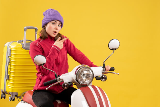 摩托车前视图：一个戴着紫色帽子的年轻女子坐在轻便摩托车上指着什么东西年轻女子指向帽子