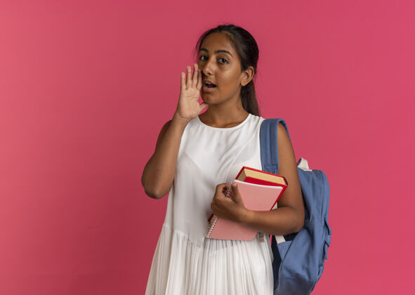 背看着镜头 年轻的女学生背着书包拿着笔记本 低声说背景粉色包