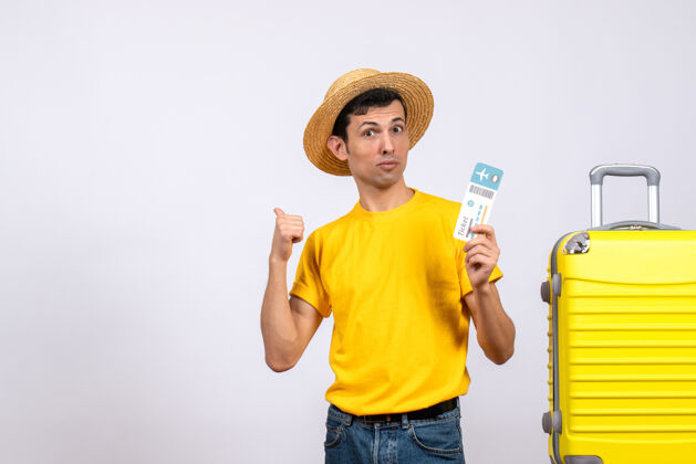 前面正面图：穿着黄色t恤的年轻人站在黄色手提箱旁 拿着票指着下面帽子票黄色