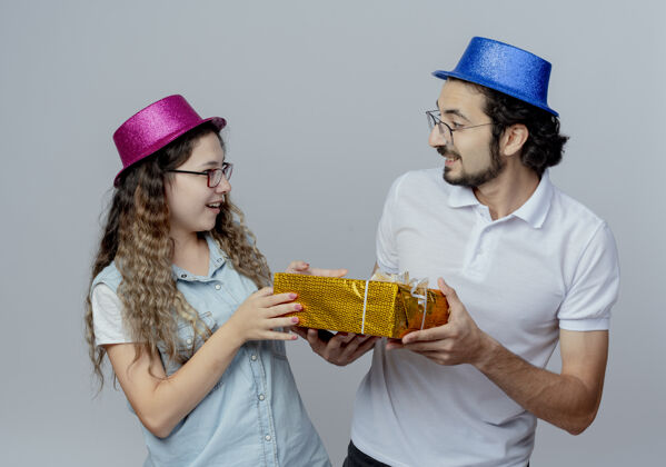 年轻高兴的小两口看着对方戴着粉蓝相间的帽子拿着礼盒盒子粉色手持