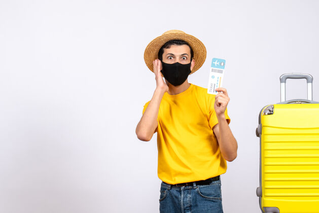 男人正面图：穿着黄色t恤的年轻人站在黄色手提箱旁 手里拿着旅行票向上休闲黄色