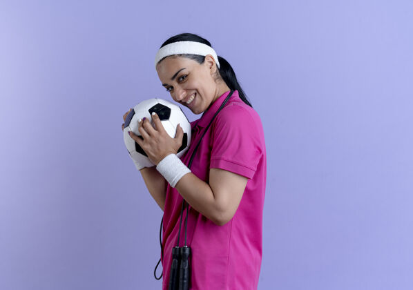 紫色年轻微笑的白人运动女性戴着头带和腕带站在一边拿着球白种人运动立场