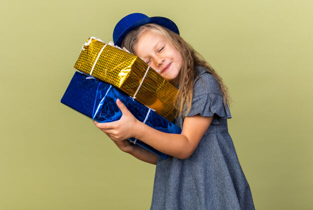 橄榄可爱的金发小女孩 戴着蓝色派对帽 头戴礼盒 孤立地放在橄榄绿的墙上 有复印空间金发孤立女孩