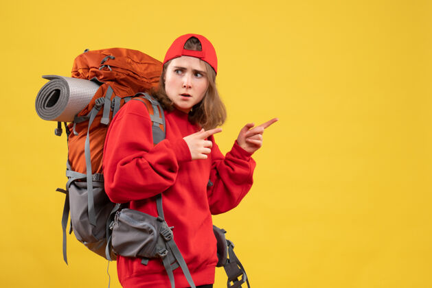 成人正面图：年轻的女旅行者背着背包指着右手手指背包前面