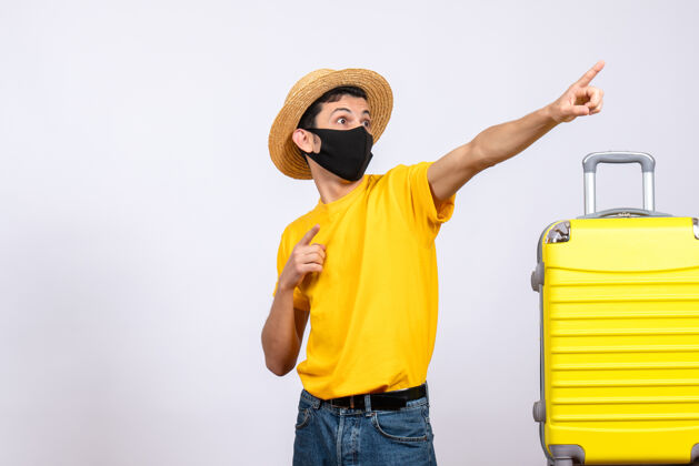 男性正面图穿着黄色t恤的年轻人站在黄色手提箱旁指着什么东西年轻人站着成人