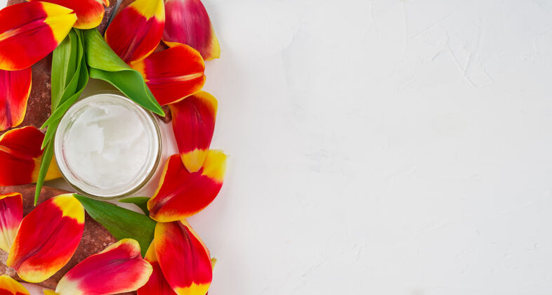 放松构图用椰子油在一个白色的罐子上围绕着郁金香花瓣 顶视图有临摹空间水平顶视图医药