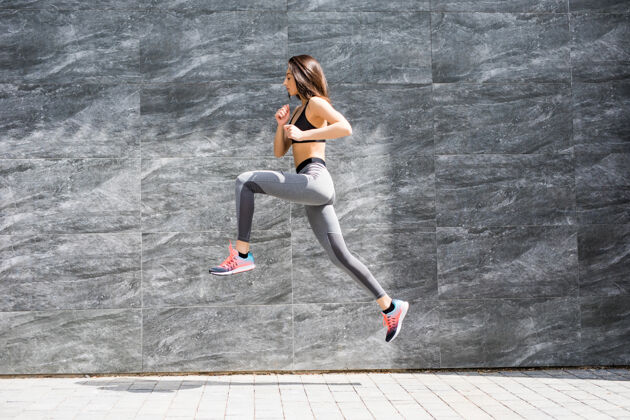 运动身体健康的年轻女子在灰色的墙壁上跳跃和奔跑物理女孩水平