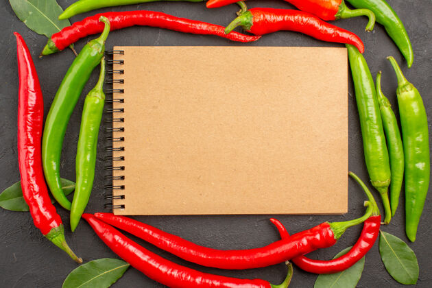 蔬菜顶视图一个笔记本在红绿的辣椒圈和黑色背景上的叶子上辣厨房辣椒
