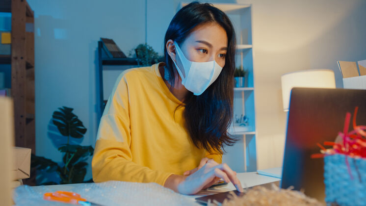 工人年轻的亚洲女商人戴着口罩在笔记本电脑上查看采购订单并回复客户收件箱聊天女性电脑电子商务
