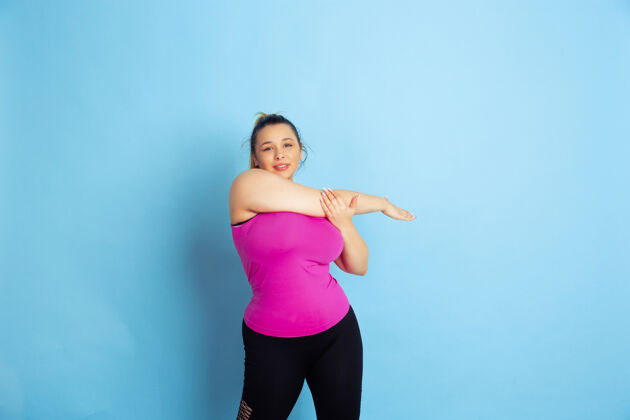 超重年轻的白人大号女模特在蓝色背景下的训练运动概念 人类情感 表达 健康的生活方式 身体积极 平等做伸展运动大小绳子饮食