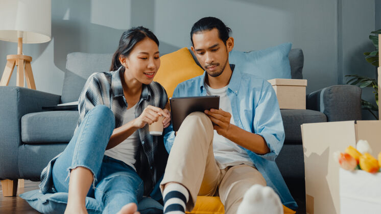 购物快乐的亚洲年轻夫妇男女用平板电脑网购家具 在新房里用纸箱包装装饰房子年轻男人抵押