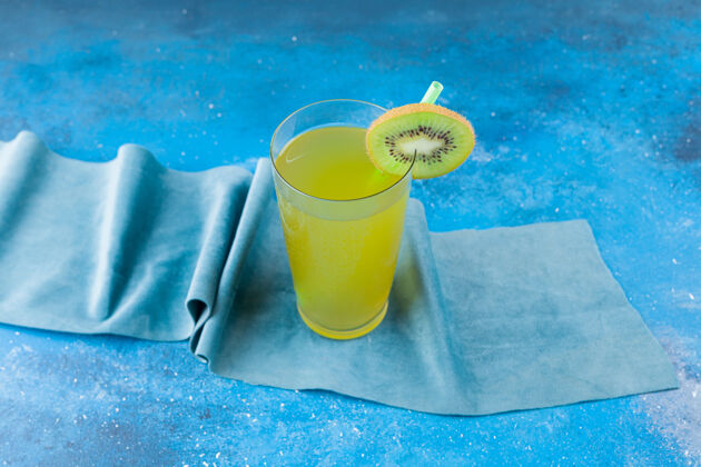 杯子在桌布上放一杯新鲜果汁和一片猕猴桃和稻草吸管切片奇异果
