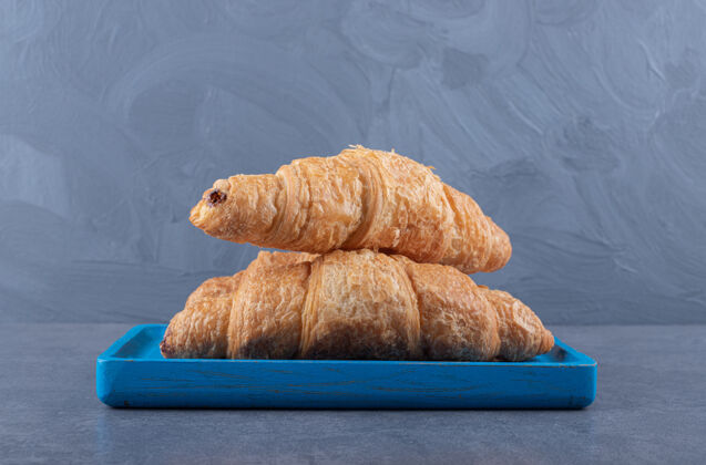 盘子新鲜的法式羊角面包 有金色的外壳放在蓝色的木板上面包早午餐羊角面包
