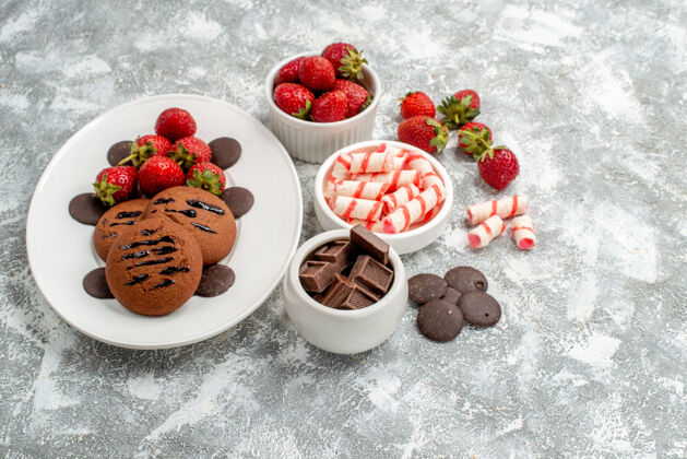 糖果白色椭圆形盘子上的饼干草莓和圆形巧克力灰白色桌子上的糖果草莓巧克力碗草莓水果碗