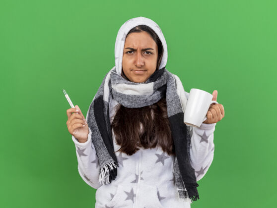 绿茶未出狱的年轻病女孩戴着头巾戴着围巾拿着温度计把一杯茶隔在绿叶上茶怀抱围巾