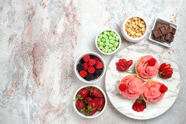 食物白色表面上有坚果和糖果的粉色草莓蛋糕俯视图胡椒饼干餐