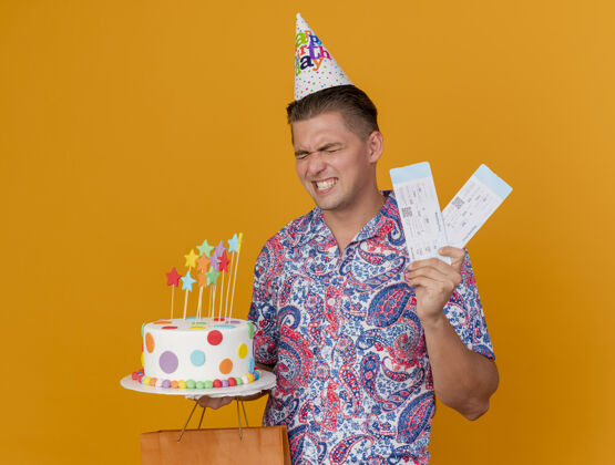 家伙快乐的年轻人戴着生日帽 手里拿着蛋糕和礼包 票子被隔离在橘子上举行穿蛋糕