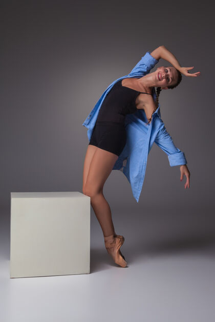 女性年轻漂亮的现代风格舞蹈演员在白色立方体上摆姿势 背景是灰色的工作室年轻活跃灵活