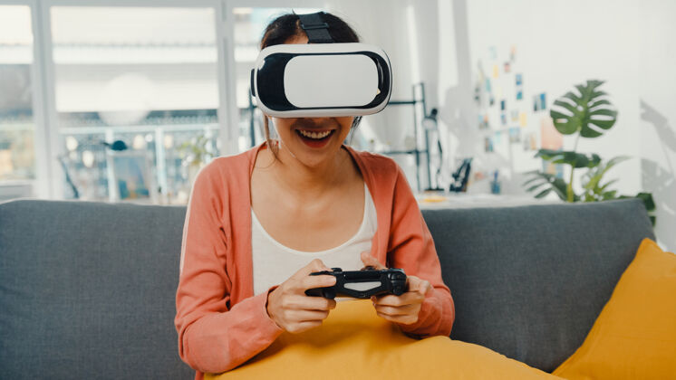 沙发亚洲女士戴着虚拟现实的耳机眼镜在客厅的沙发上玩游戏杆虚拟远程现实